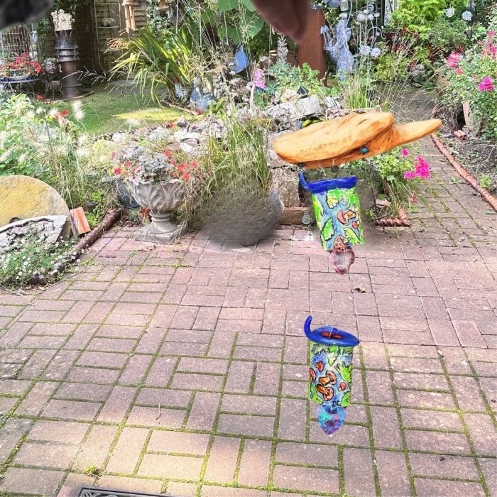 Handmade toadstool mobile with embossed decorations on driftwood support, suspended by a weatherproof cord."