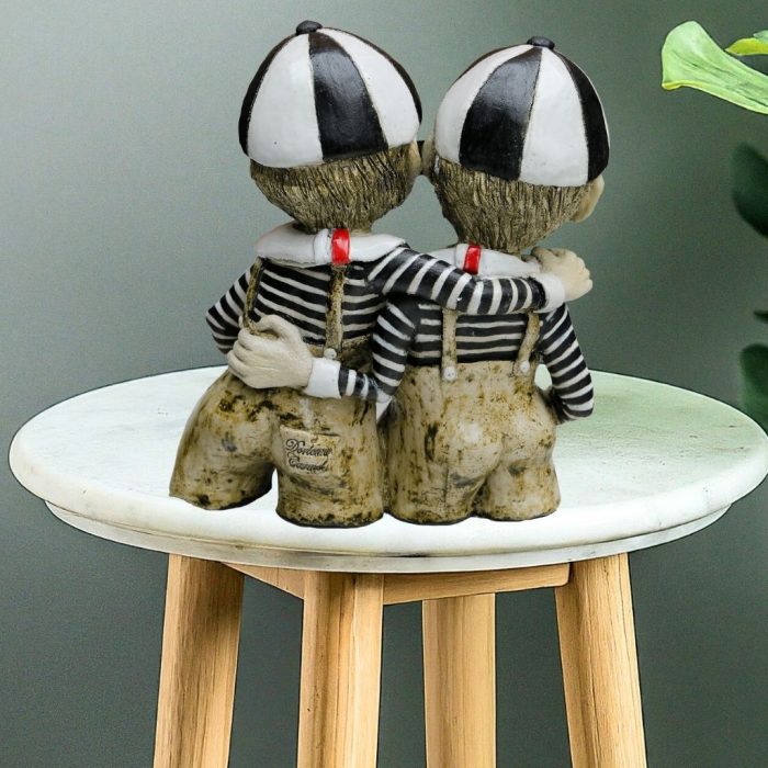 This handcrafted ceramic sculpture features Tweedle Dum and Tweedle Dee dressed in black-and-white striped tops, red ties, beige trousers, and matching school caps, showcasing brotherly love and playful charm.
