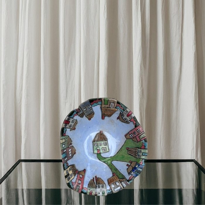 "Colourful village scene"-This handmade food-safe bowl features colourful, uniquely shaped houses. A pathway leads to a central house on a light blue surface, and some houses are raised for texture.