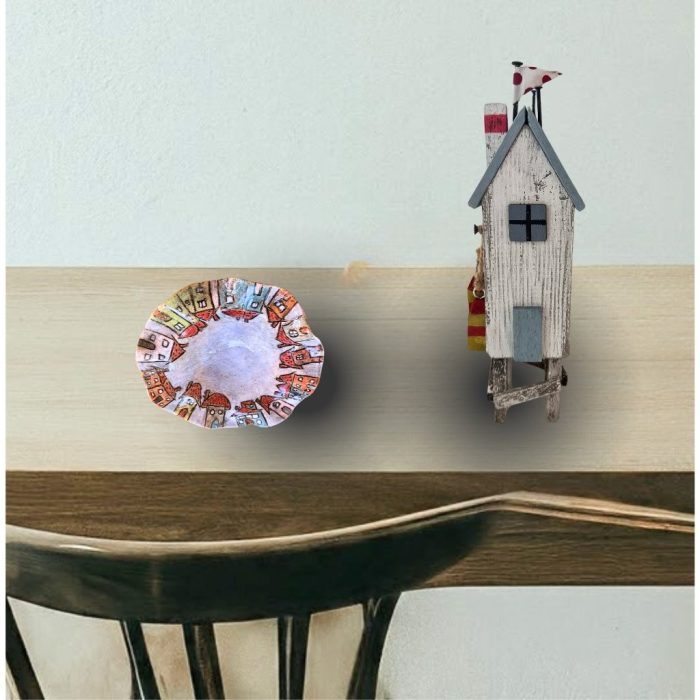 This charming handmade ceramic dish has wavy edges that showcase colourful houses and a warm red heart. It is perfect for decorative or serving use.
