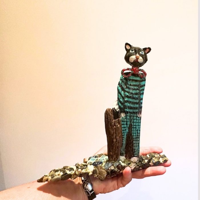 Handmade ceramic cat sculpture with a driftwood post and textured stone base.