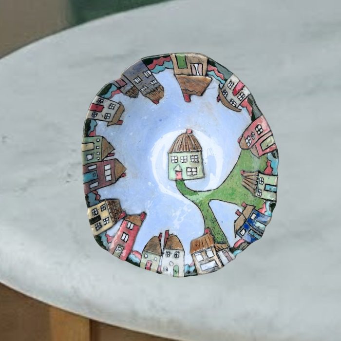 "Colourful village scene"-This handmade food-safe bowl features colourful, uniquely shaped houses. A pathway leads to a central house on a light blue surface, and some houses are raised for texture.