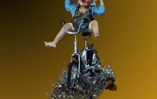 Ceramic figure of a woman with wire curly hair, raising her arms joyfully while cycling, set on a textured grassy ceramic base.